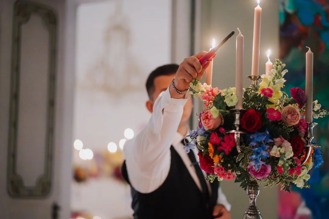 Mann in formeller Kleidung zündet Kerzen auf einem Blumenarrangement an.