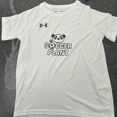 White T-shirt with Under Armour logo and a graphic of a panda bear with soccer ball, and the text 'Soccer Plant'.