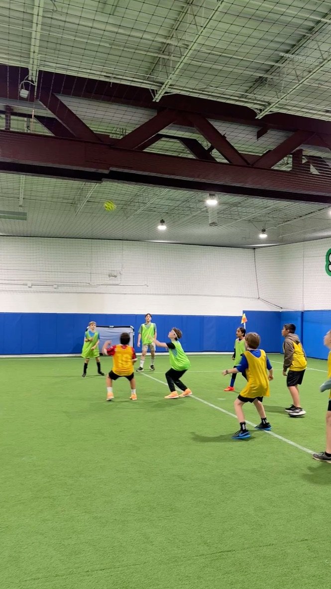 Children playing a game of indoor soccer inside a sports facility.