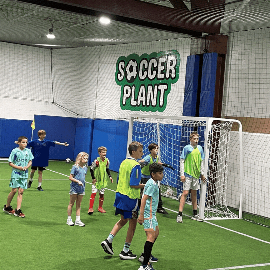 Children playing indoor soccer with a goal and a net, under a sign that reads 'Soccer Plant'.