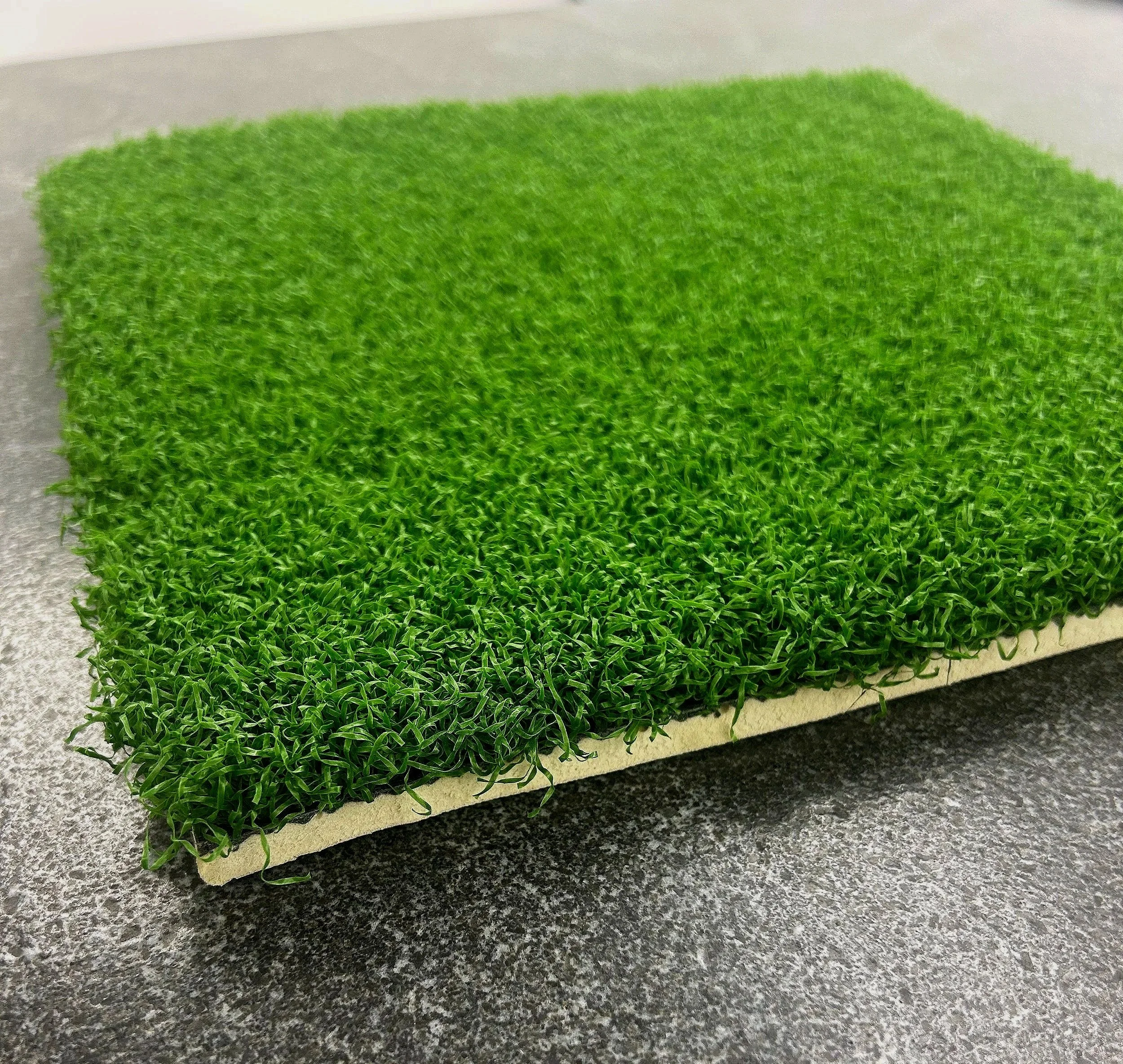 Close-up of a green artificial grass mat on a dark gray surface.