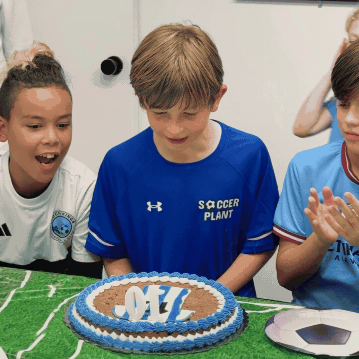 Children celebrating a soccer-themed birthday party with a cake decorated in blue, white, and brown, featuring a pennant with the number 10 on top.