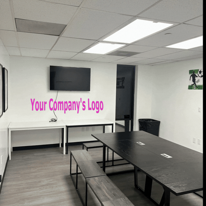 Empty conference room with a large TV screen, a table with attached electrical outlets, benches, a wall logo, and a trash bin.