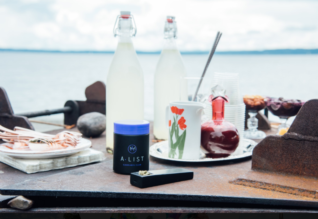 Table set outdoors near a body of water with bottles, glasses, a pitcher, and decorative items.