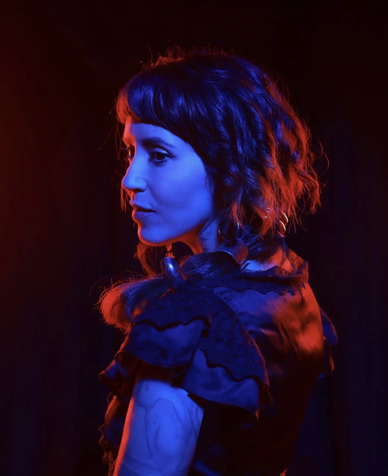 Side profile of a woman with short, curly hair illuminated by red and blue lights against a dark background.