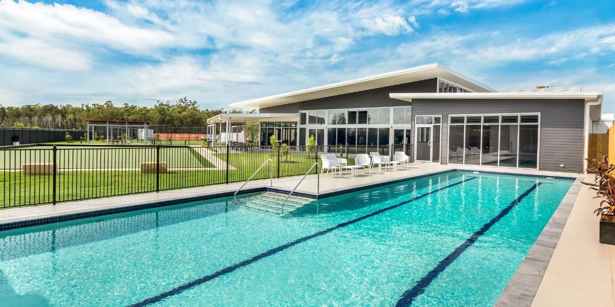 Modern house with a backyard pool, poolside seating, green lawn, and a fence, under a partly cloudy sky.