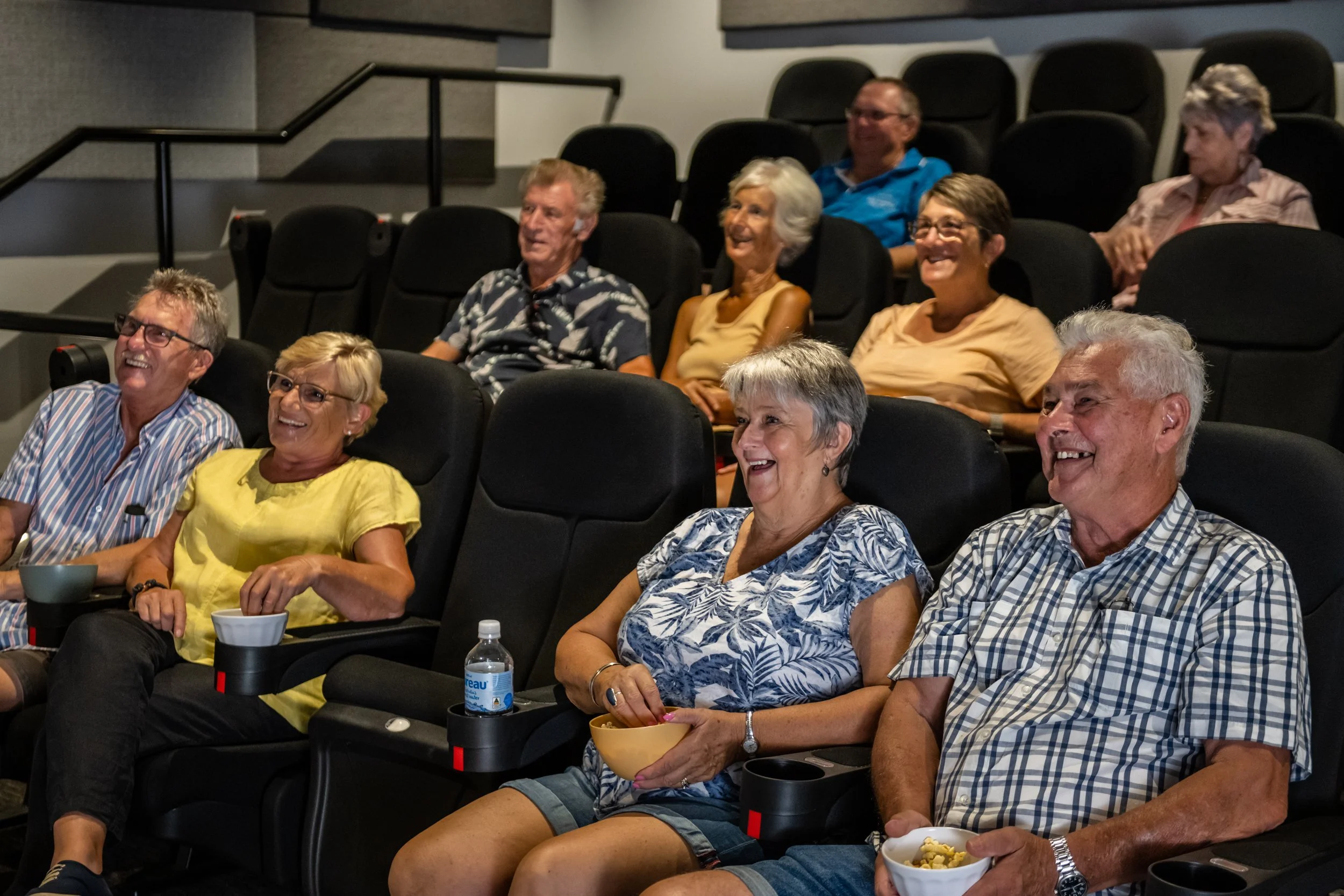 A group of elderly people sitting in a movie theater, smiling and watching a film.