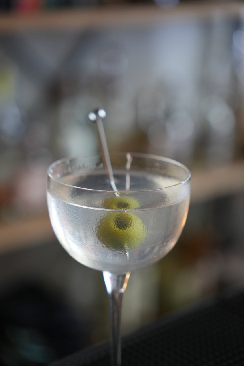 A dirty martini in a cocktail glass with an olive on a skewer.