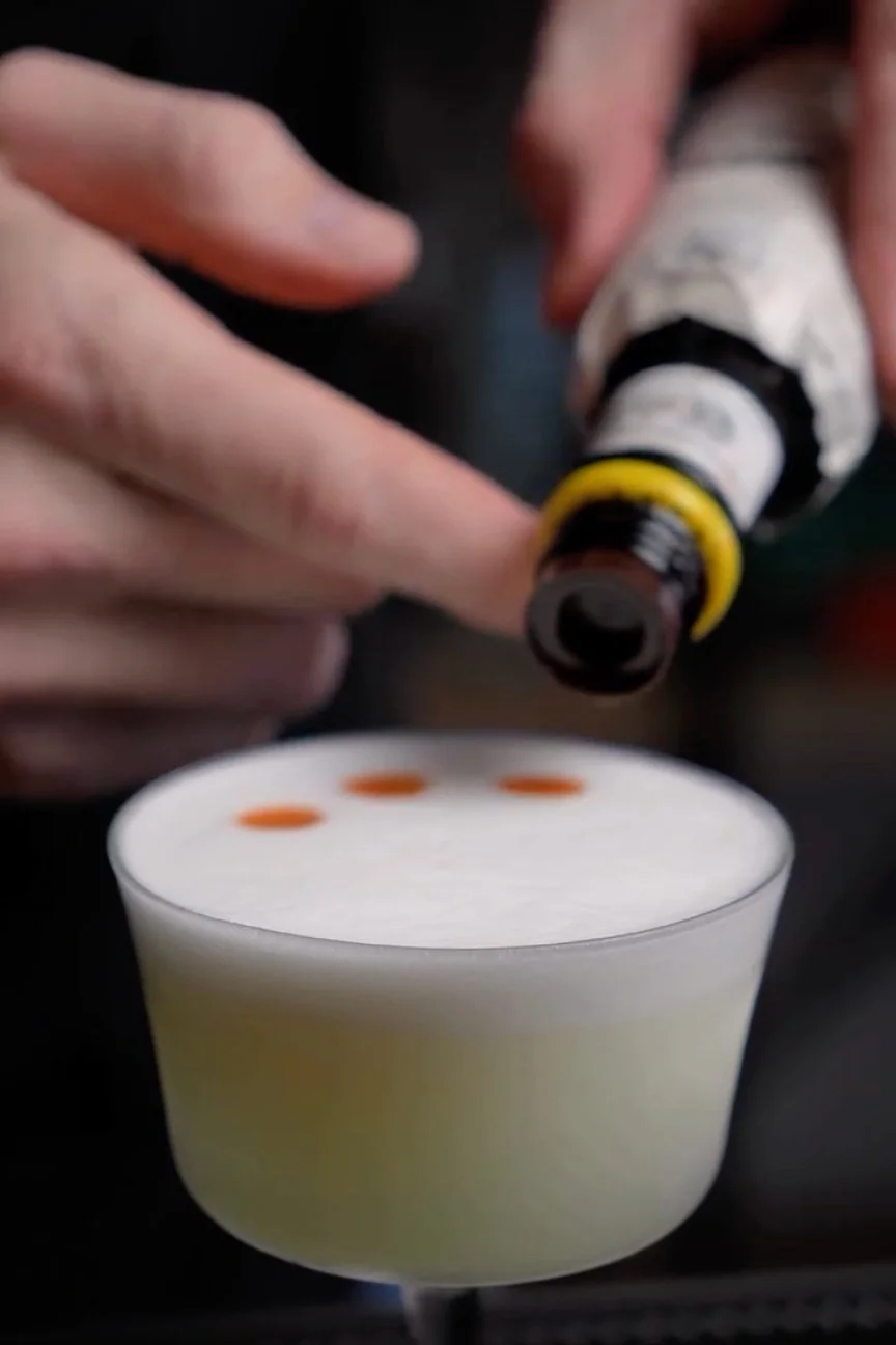 How to garnish a whiskey sour with Angostura bitters drops on top off egg white foam