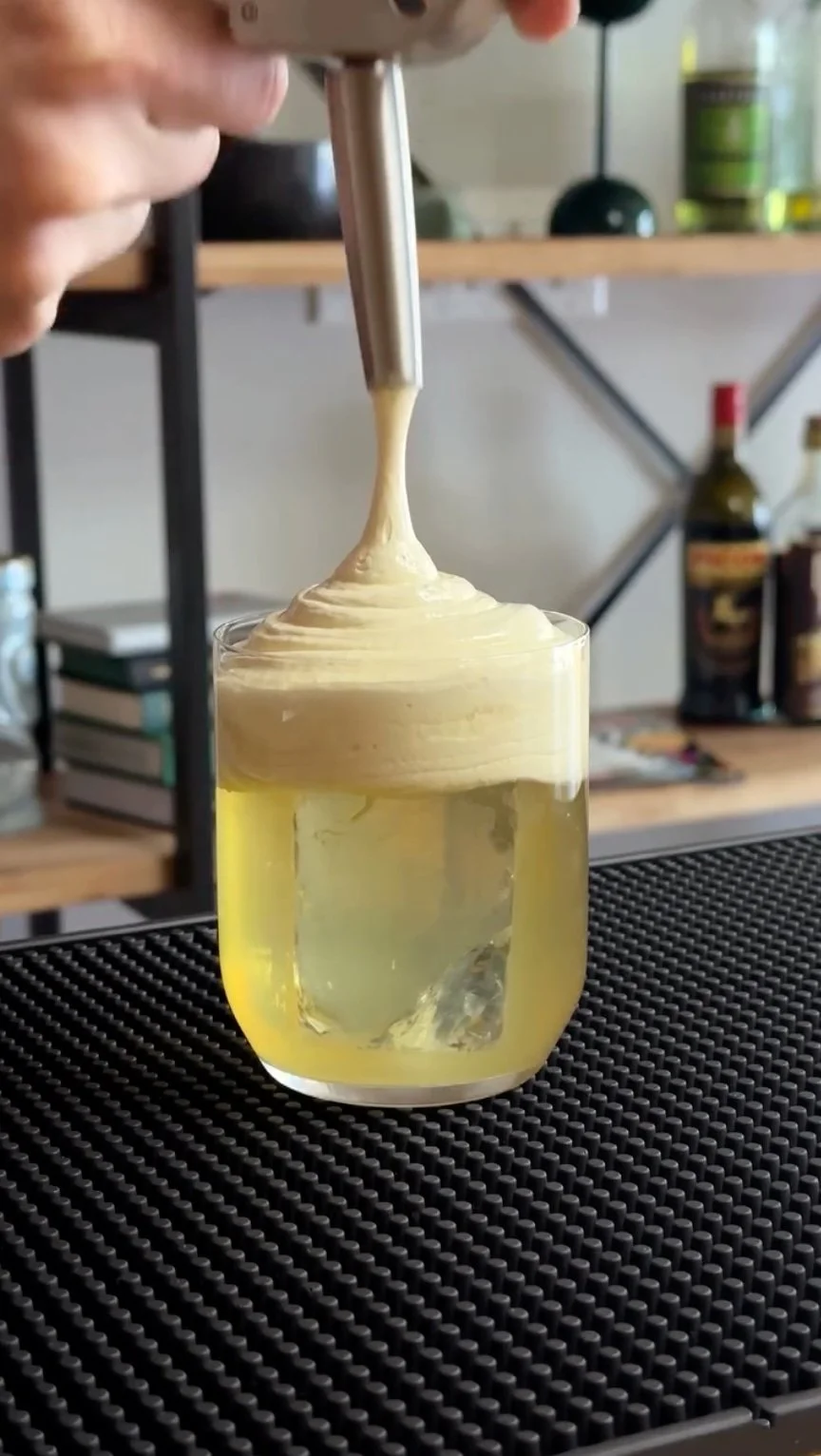Pouring iSi cocktail foam onto a clarified cocktail
