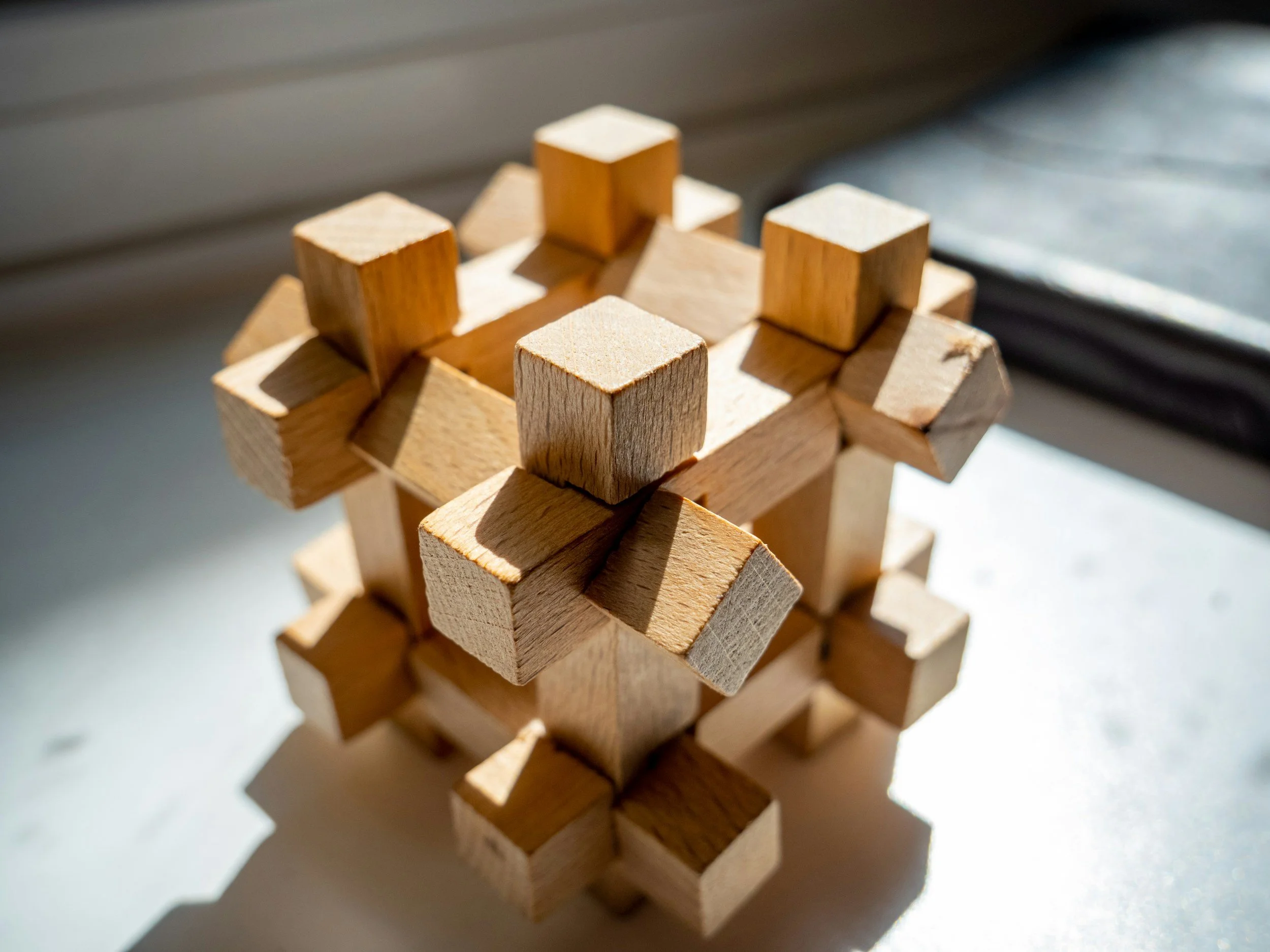 Close-up of a geometric wooden structure with interlocking square and rectangular blocks, illuminated by sunlight.