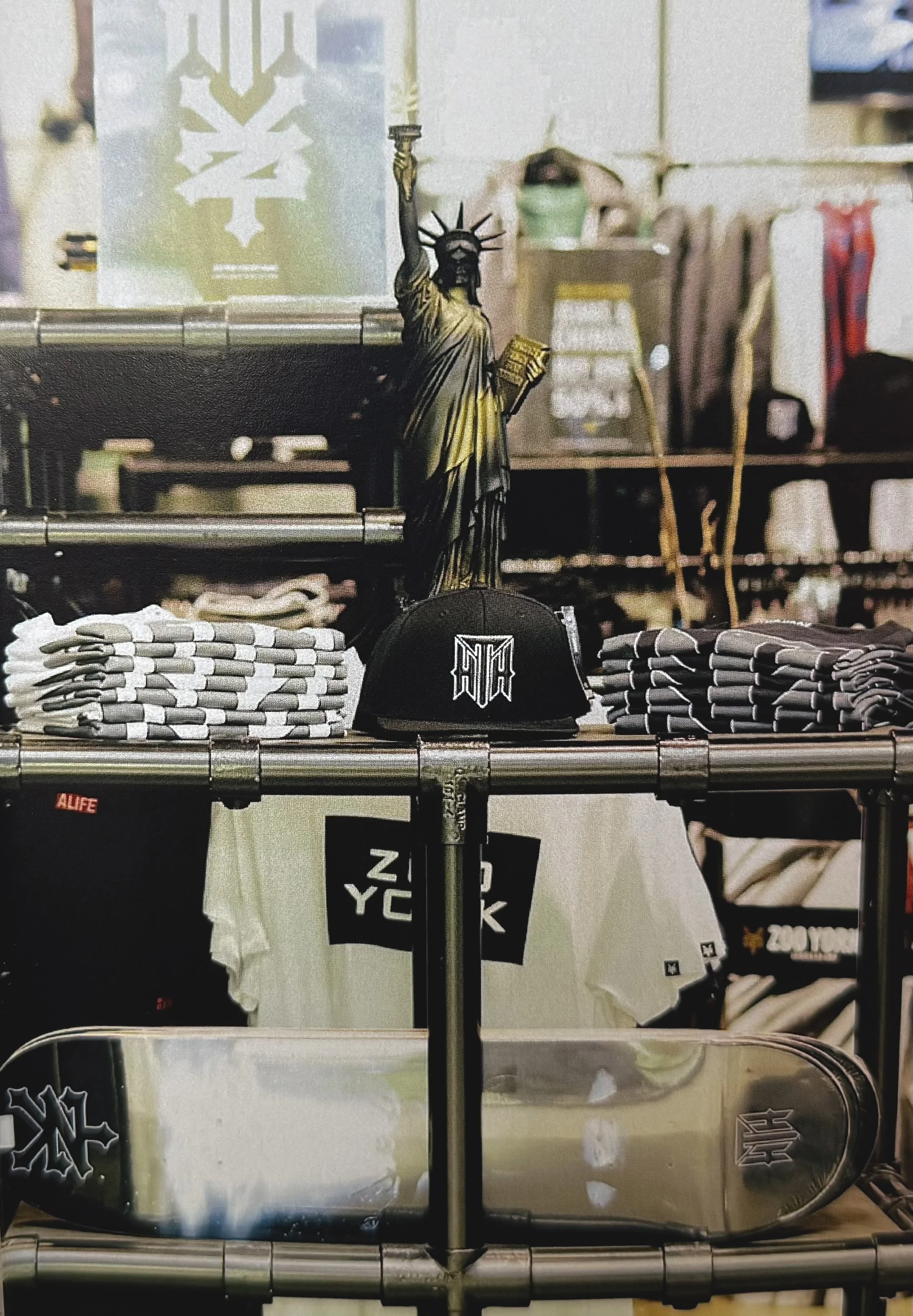 A display of various merchandise items on a store shelf, including a small replica of the Statue of Liberty, folded clothing, hats, and other accessories.