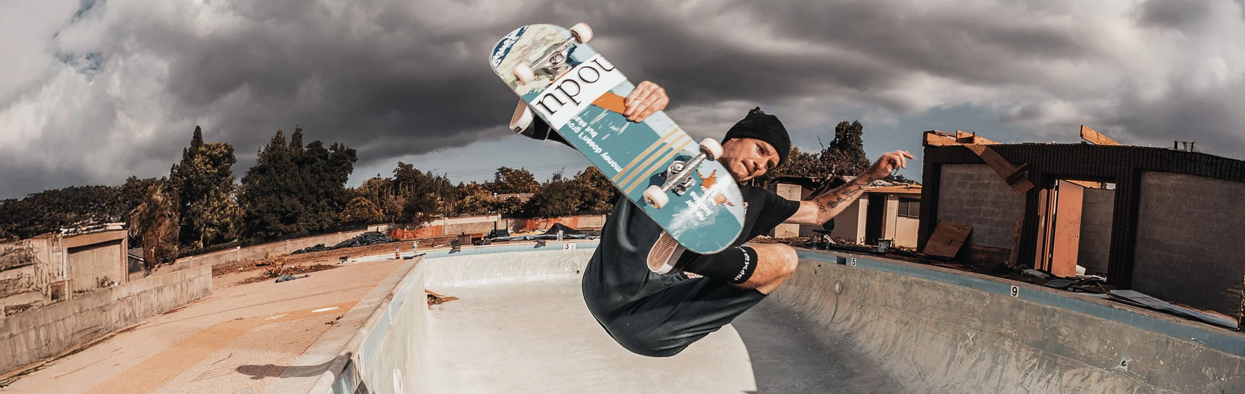 A skateboarder performing an aerial trick in an empty swimming pool on a cloudy day.