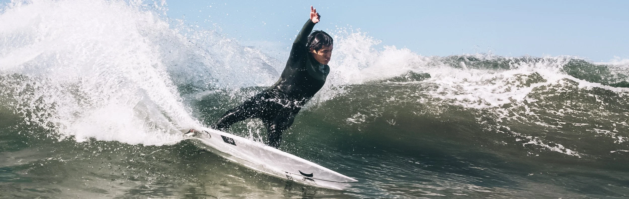 Person in black wetsuit surfing on a white surfboard on a wave.