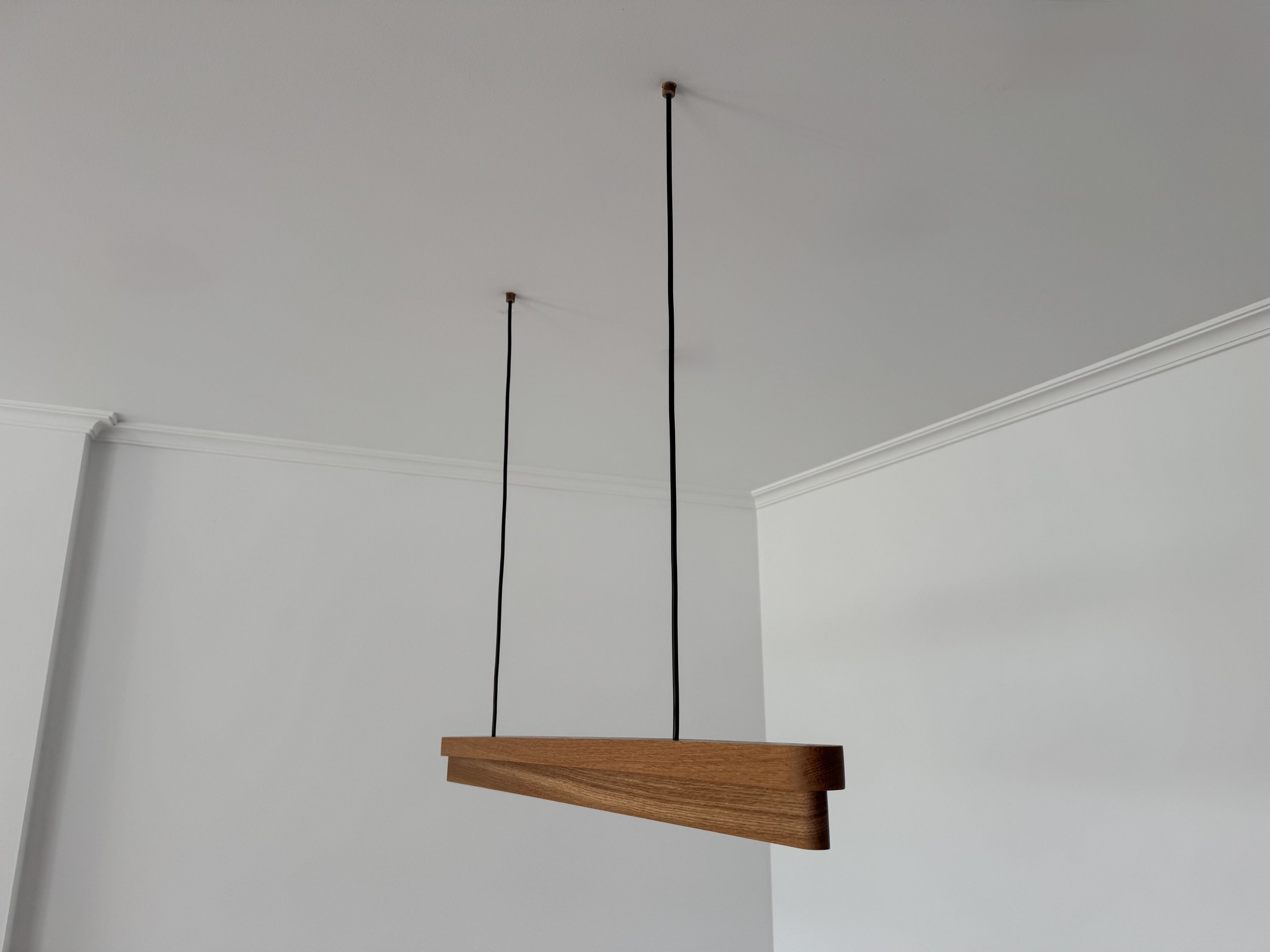 Lámpara de techo moderna hecha de madera suspendida con cables negros en un techo blanco.