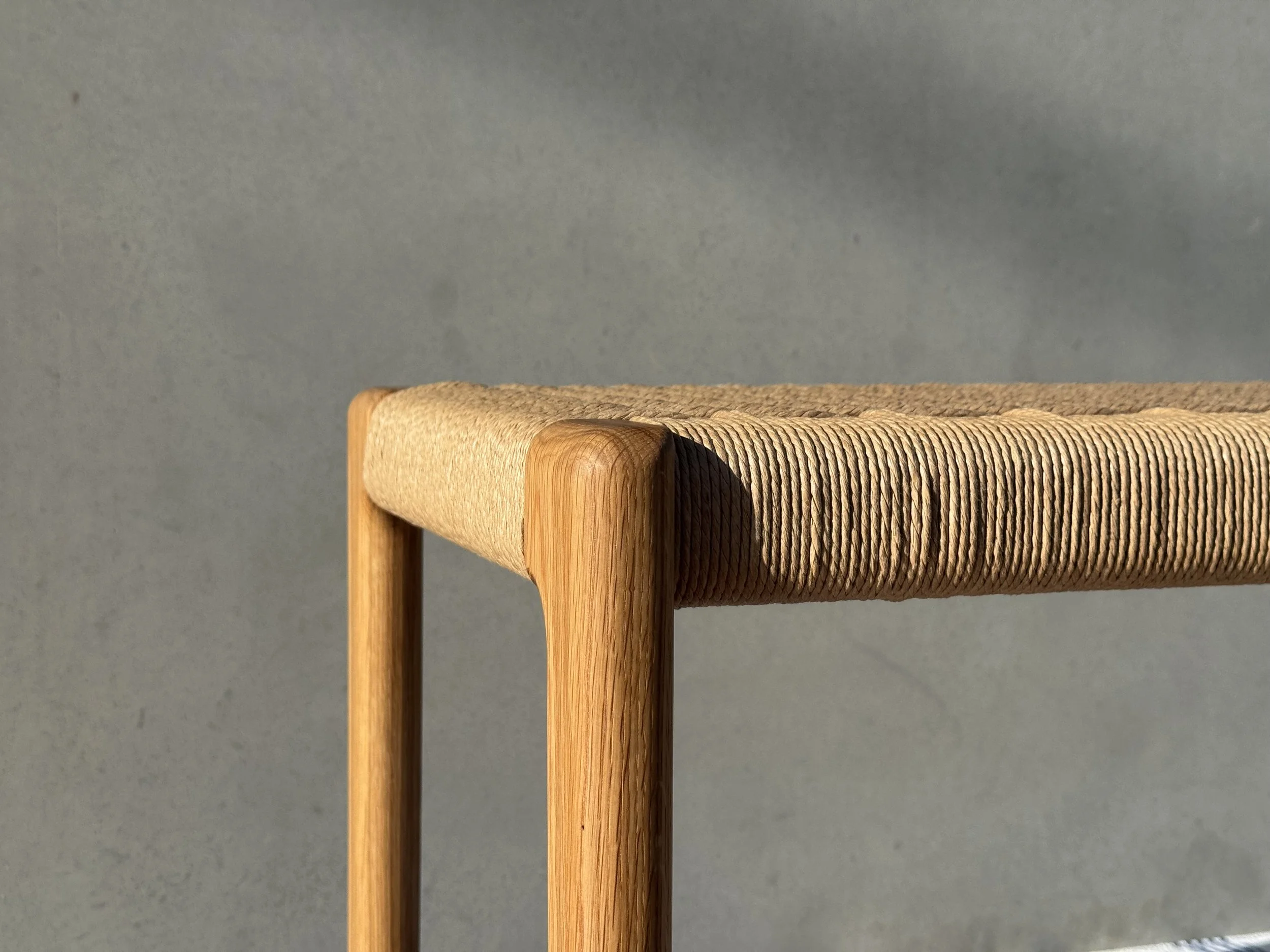 Banco de madera y cuerda en un espacio con pared gris.