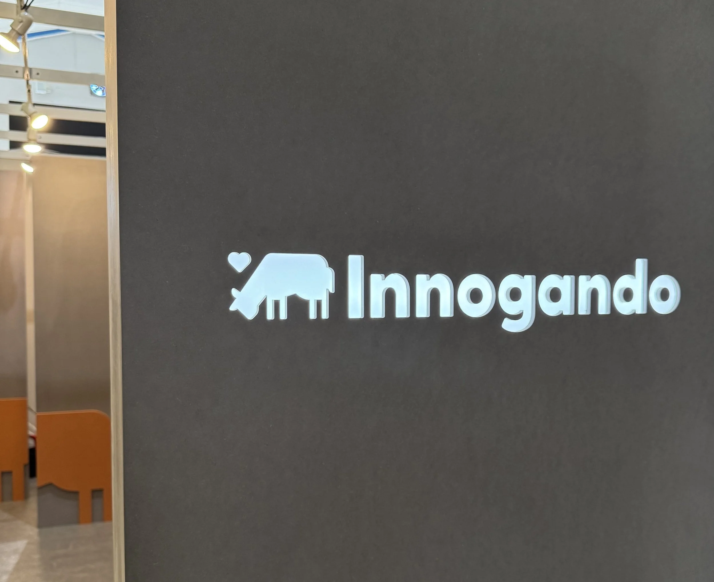 Se ve un cartel con el logotipo de Inmobiliaria, una casa y un corazón, en un entorno interior con paredes negras, luminarias en el techo y un espacio de exhibición.