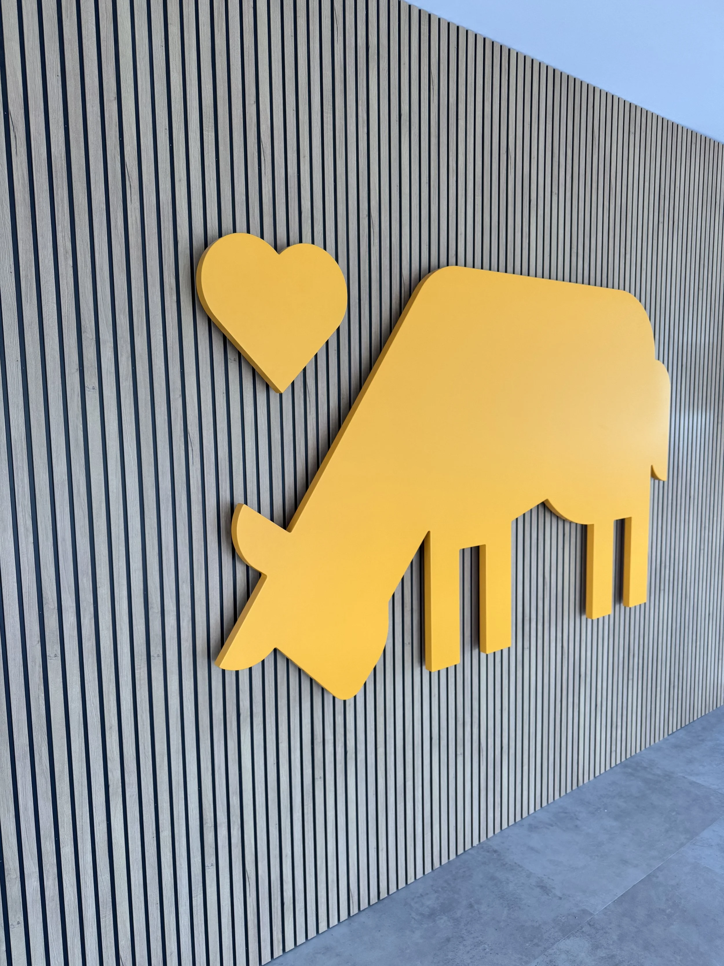 Este es un logotipo de una mano y un corazón de color amarillo, colocado en una pared de listones de madera