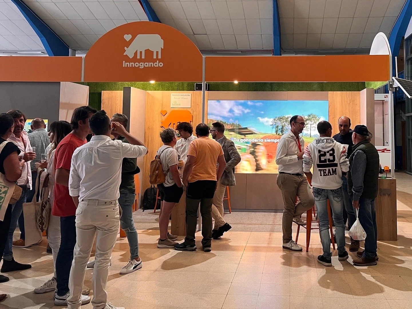 Grupo de personas en un stand de exhibición de productos agrícolas, con logo de Innogando y pantalla digital que muestra imágenes y texto sobre ganadería.