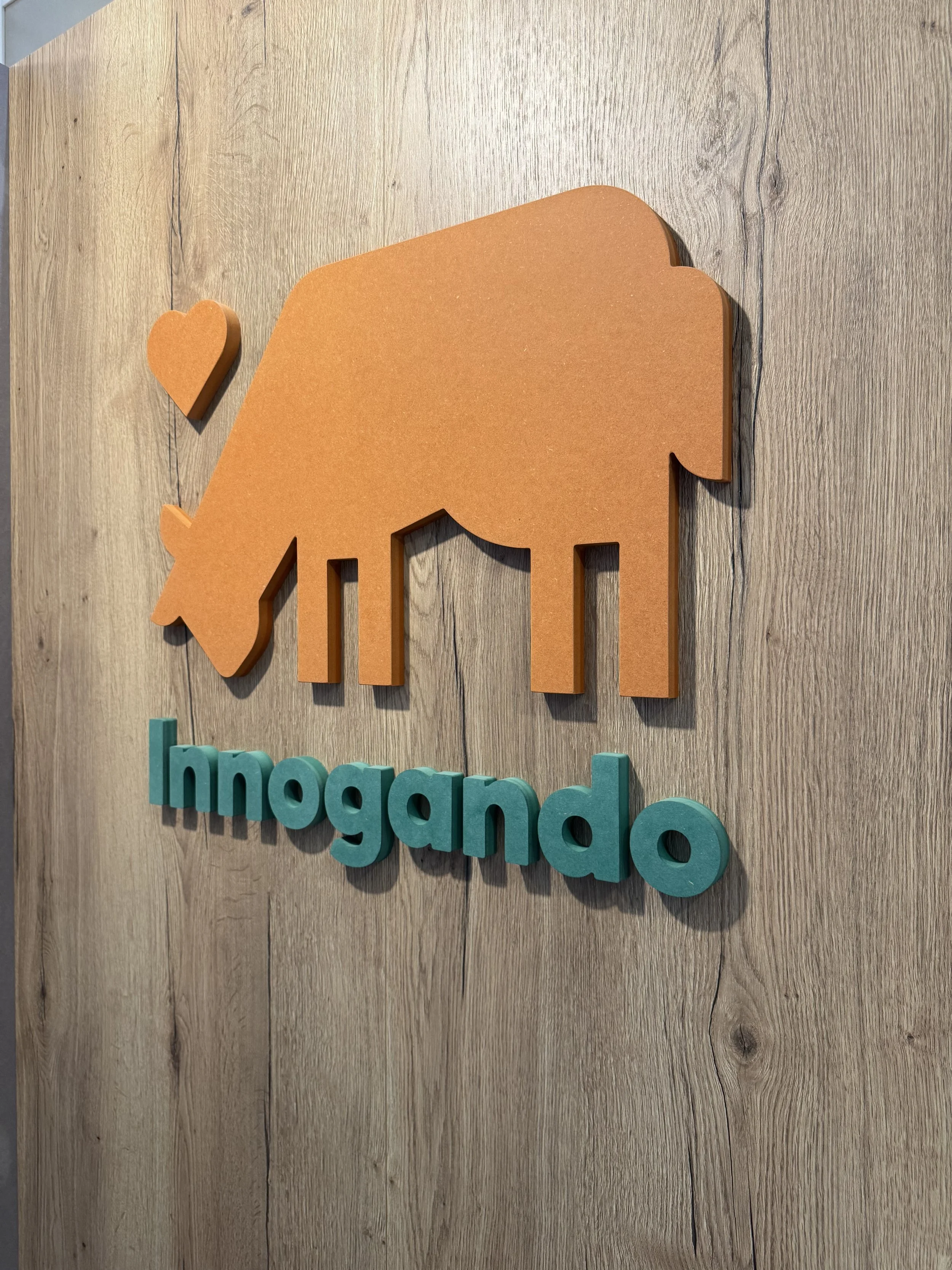 Signo de madera en forma de elefante de color naranja y corazón en un fondo de madera con las palabras 'Inagando' en letras azules.