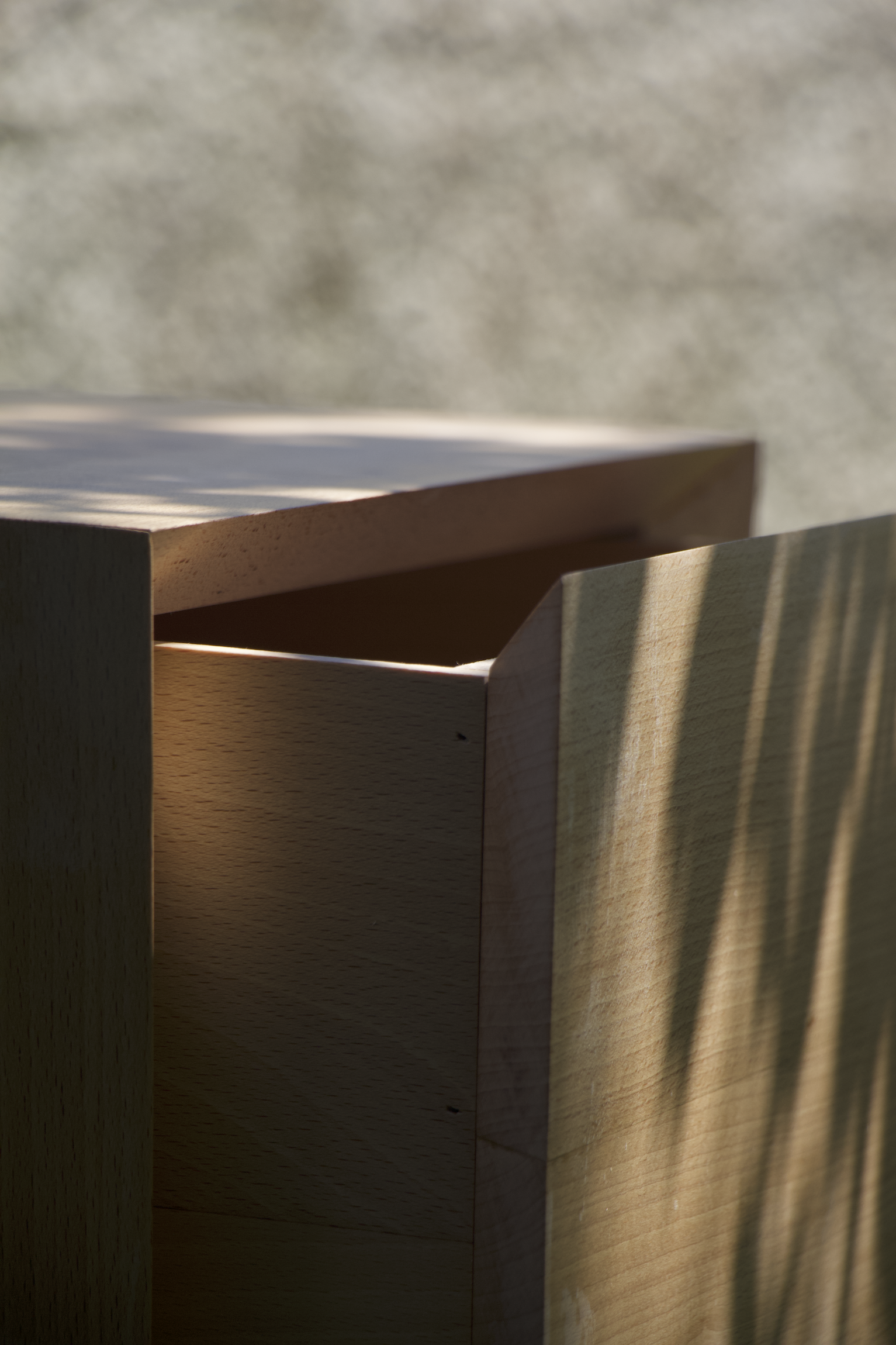 Primer plano de una mesa de noche de madera, con sombra de hojas sobre la superficie, en un clima soleado.
