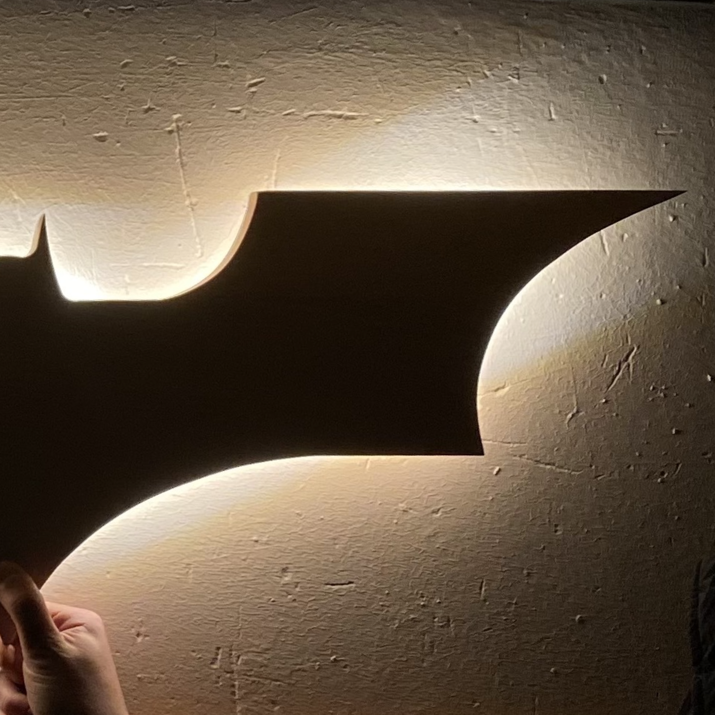 Una figura de madera en forma de murciélago, iluminada desde atrás, colocada en una pared.