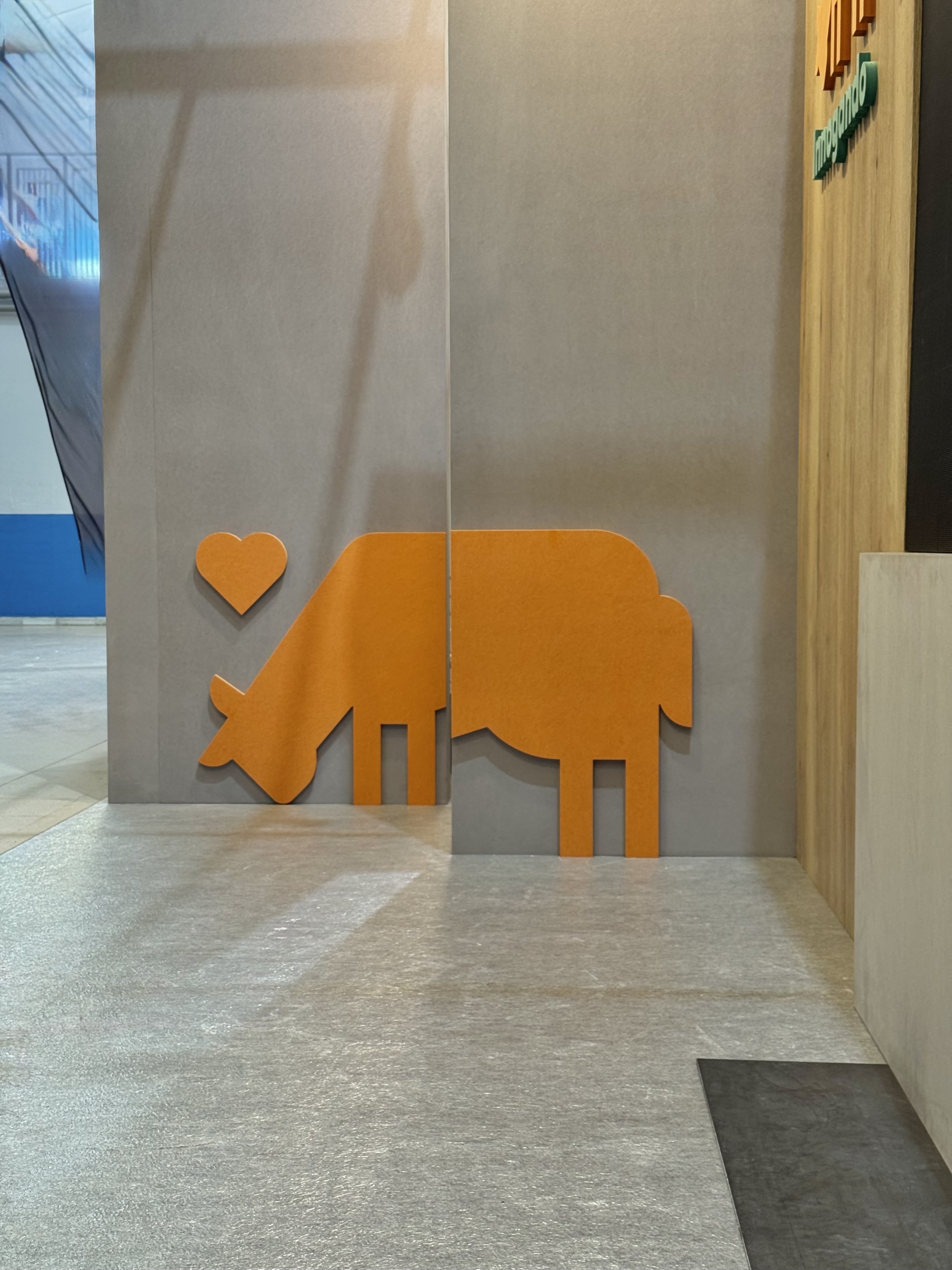 pared con decoraciones en color naranja y una figura de elefante, en un espacio interior con suelo de textura gris y un muro de madera a la derecha.