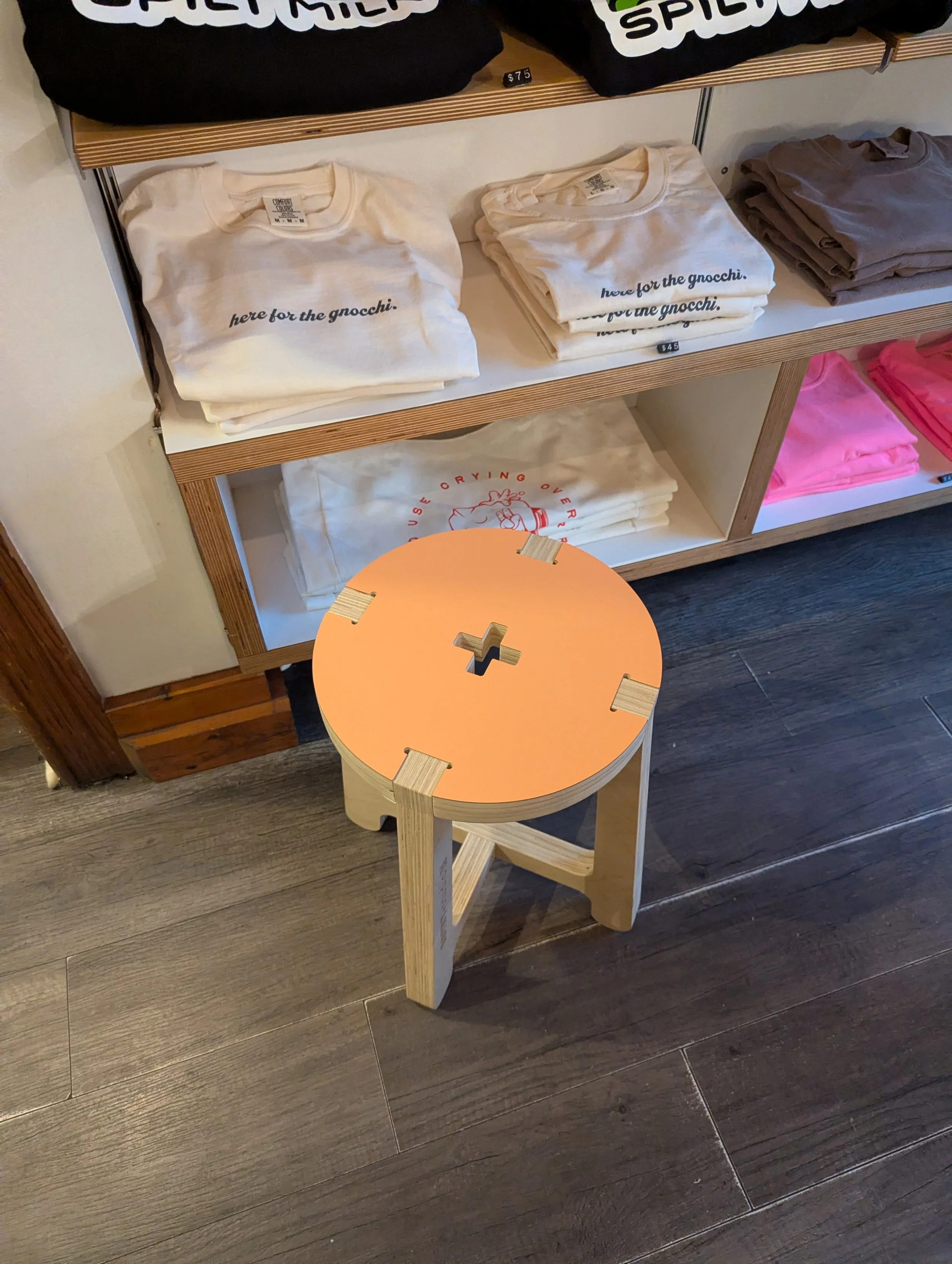 Display of folded T-shirts on shelves with a small wooden stool in front.