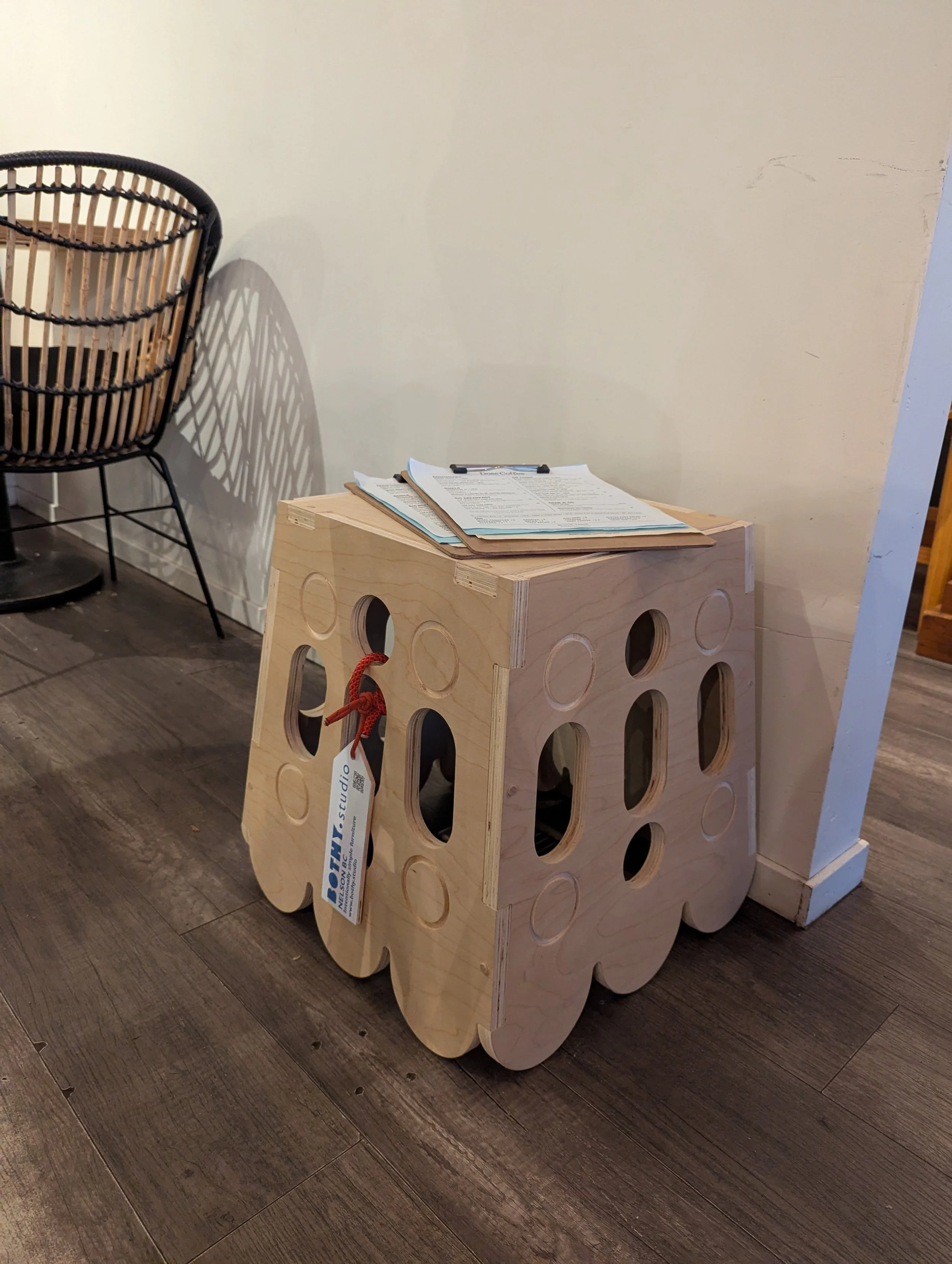 A wooden skull-shaped side table with a clipboard and papers on top, situated near a black chair on a dark hardwood floor.