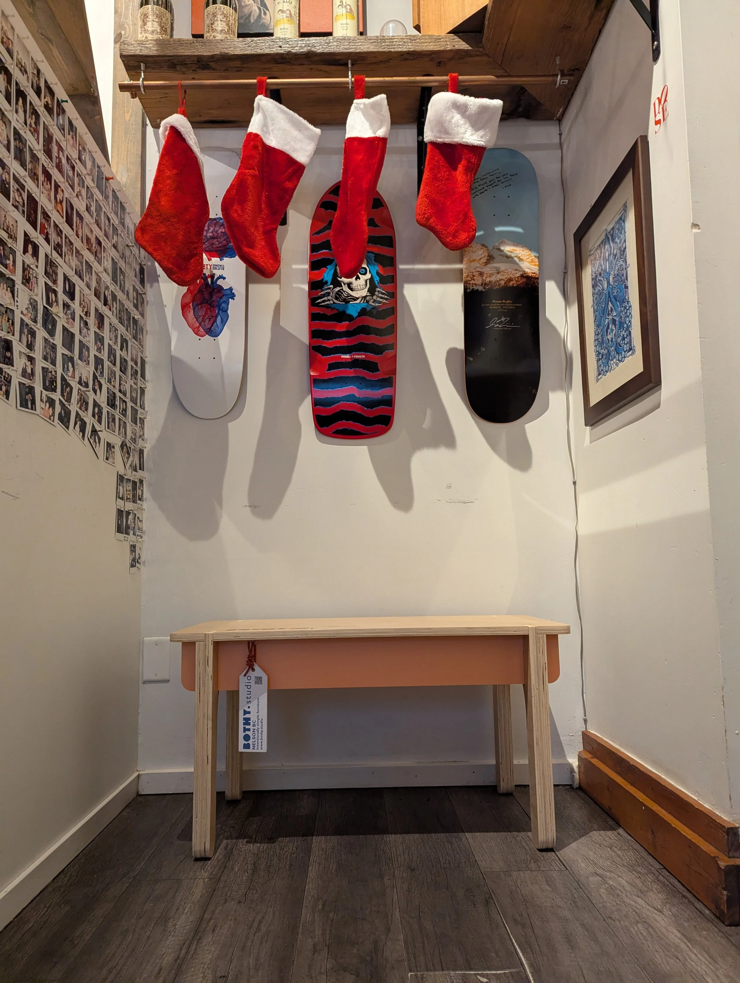 Four red and white Christmas stockings hanging from a wooden rod, three skateboards mounted on the wall behind them, and a framed picture on the right wall in a cozy indoor space.