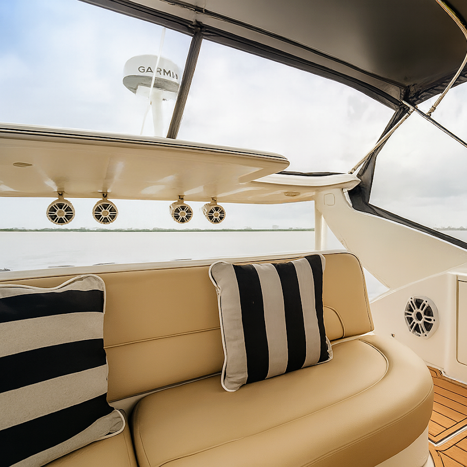 Interior of a boat with cream-colored seating, striped pillows, and a view of a Garmin radar on the top deck through the windows.