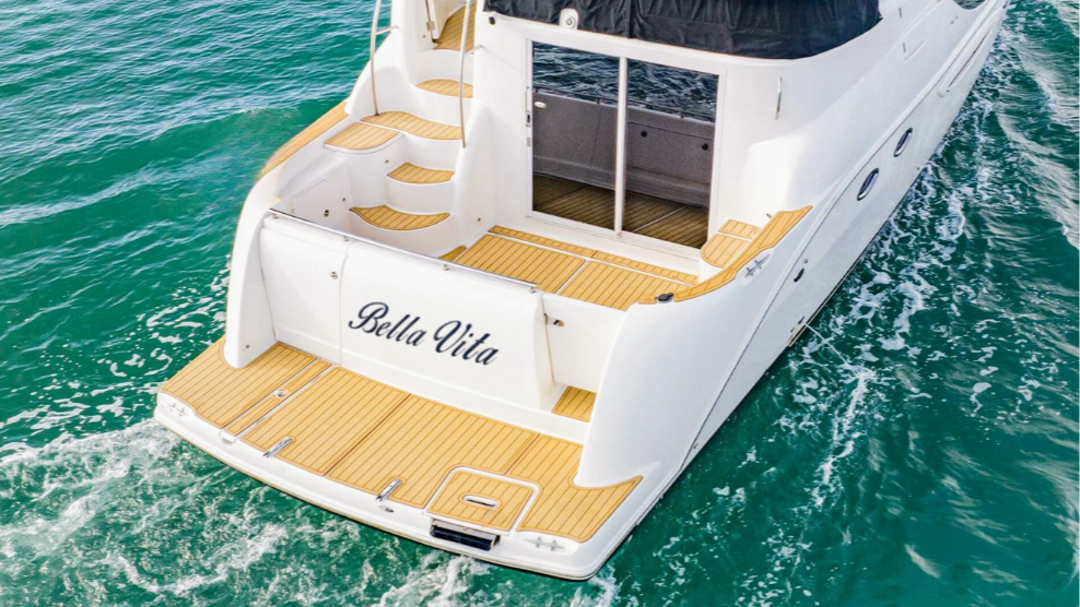 An aerial view of a luxury white yacht with a wooden deck, named Bella Vita, floating in the ocean.