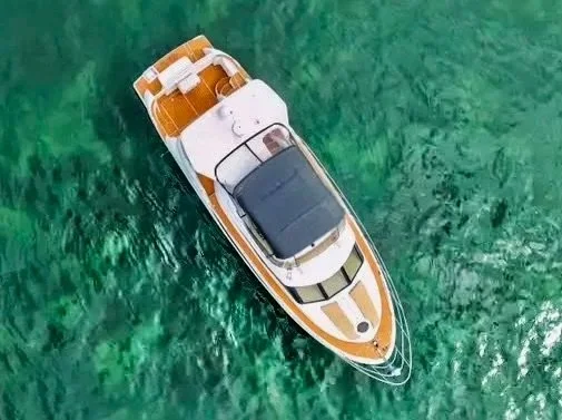 Overhead view of a white and brown yacht floating on clear green water.
