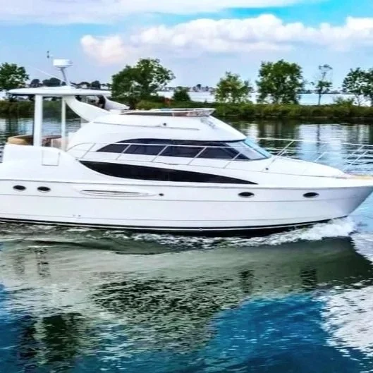 A white luxury yacht cruising on a calm body of water with trees and a partly cloudy sky in the background.