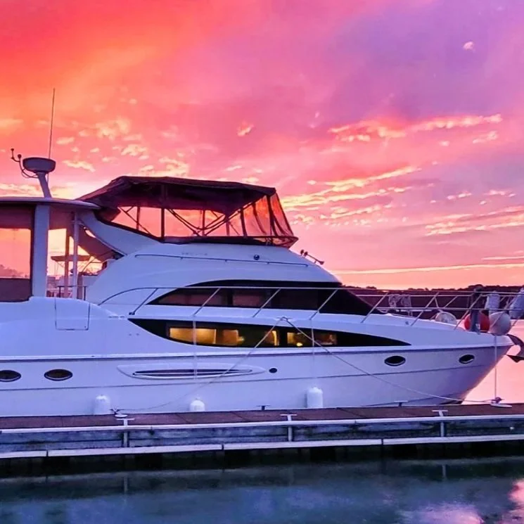 A white yacht docked at a pier during a colorful sunset with pink, purple, and orange sky.