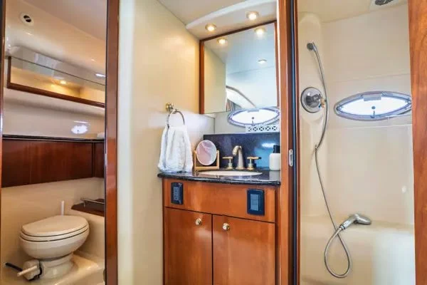 Bathroom on a boat with a toilet, sink with faucet, mirror, towel, and a shower area with a small window.