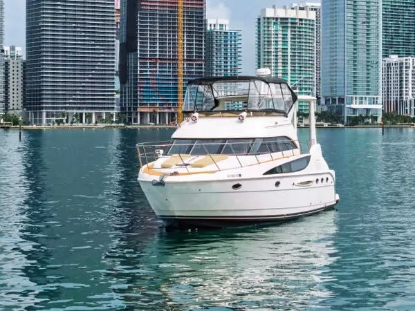 A white yacht anchored in a marina with modern high-rise buildings in the background.