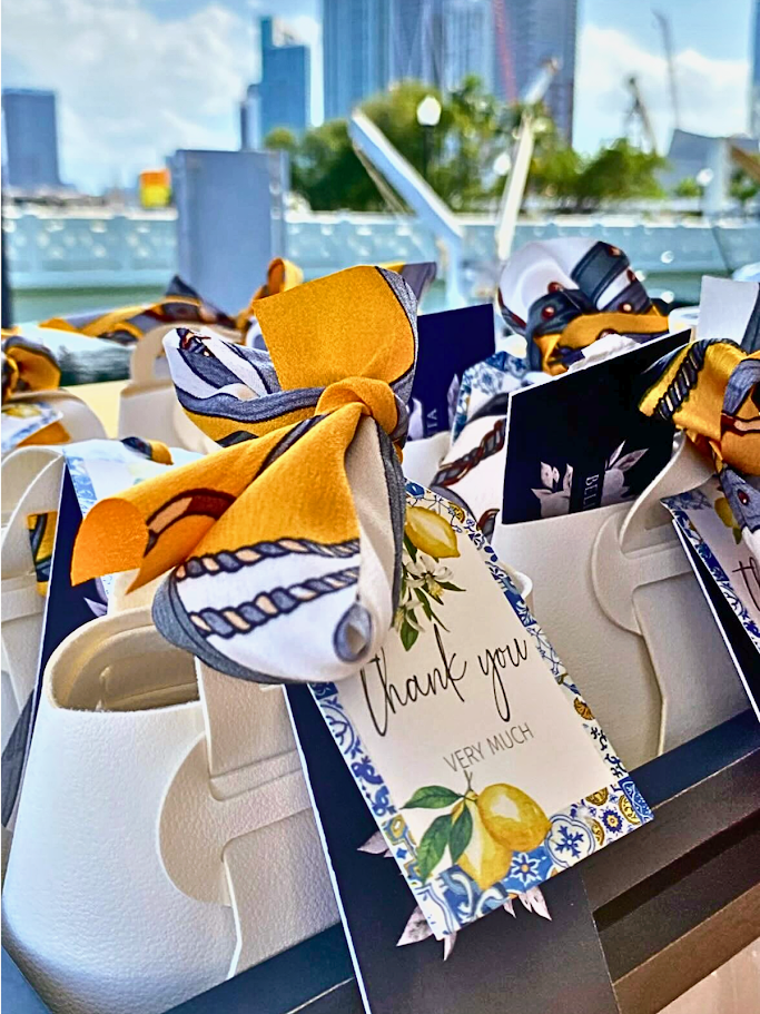 Thank you cards tied with yellow and patterned silk scarves on a white foam tray, with a cityscape in the background.
