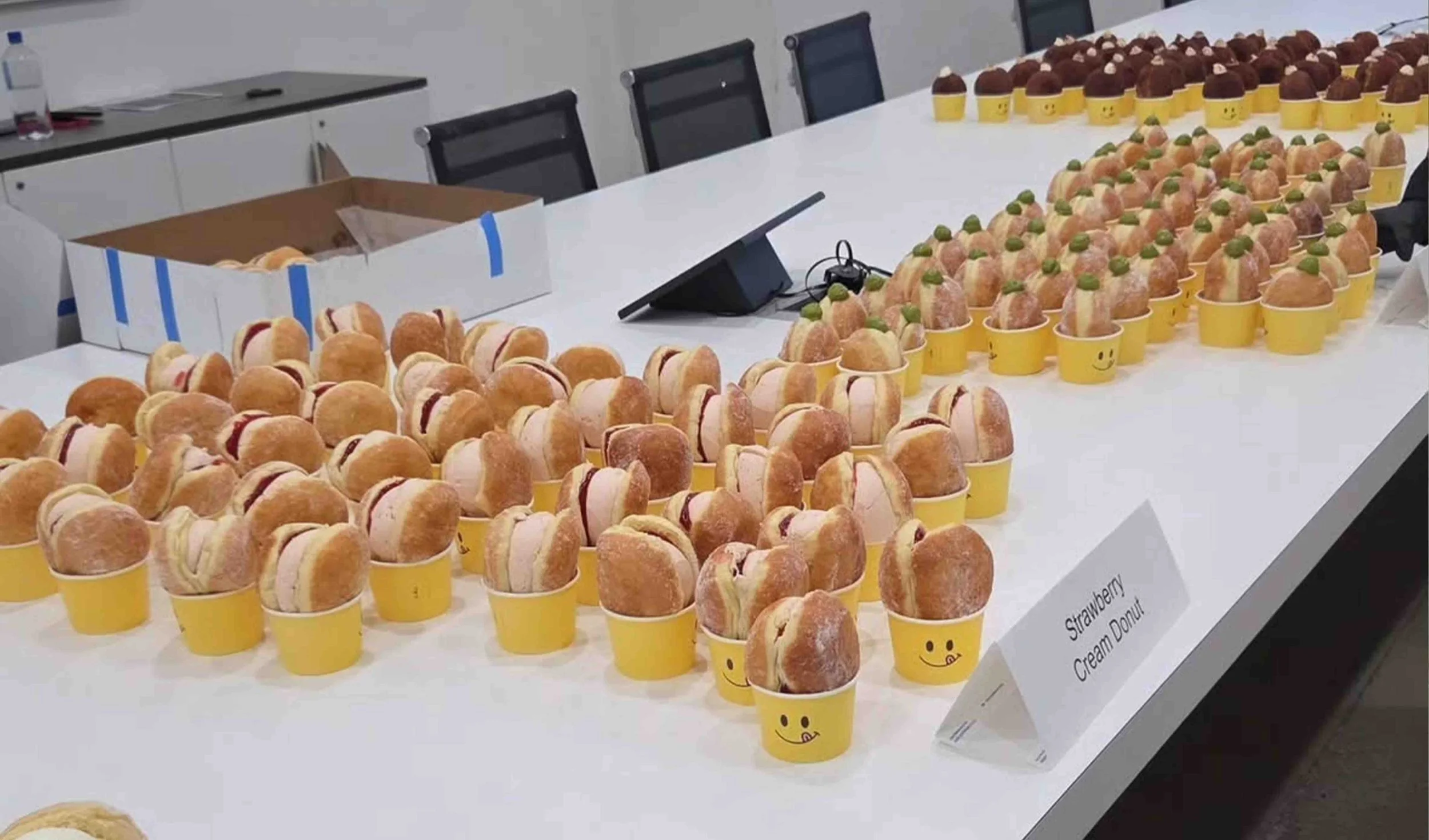Assorted donuts in yellow smiley-face cups for corporate catering