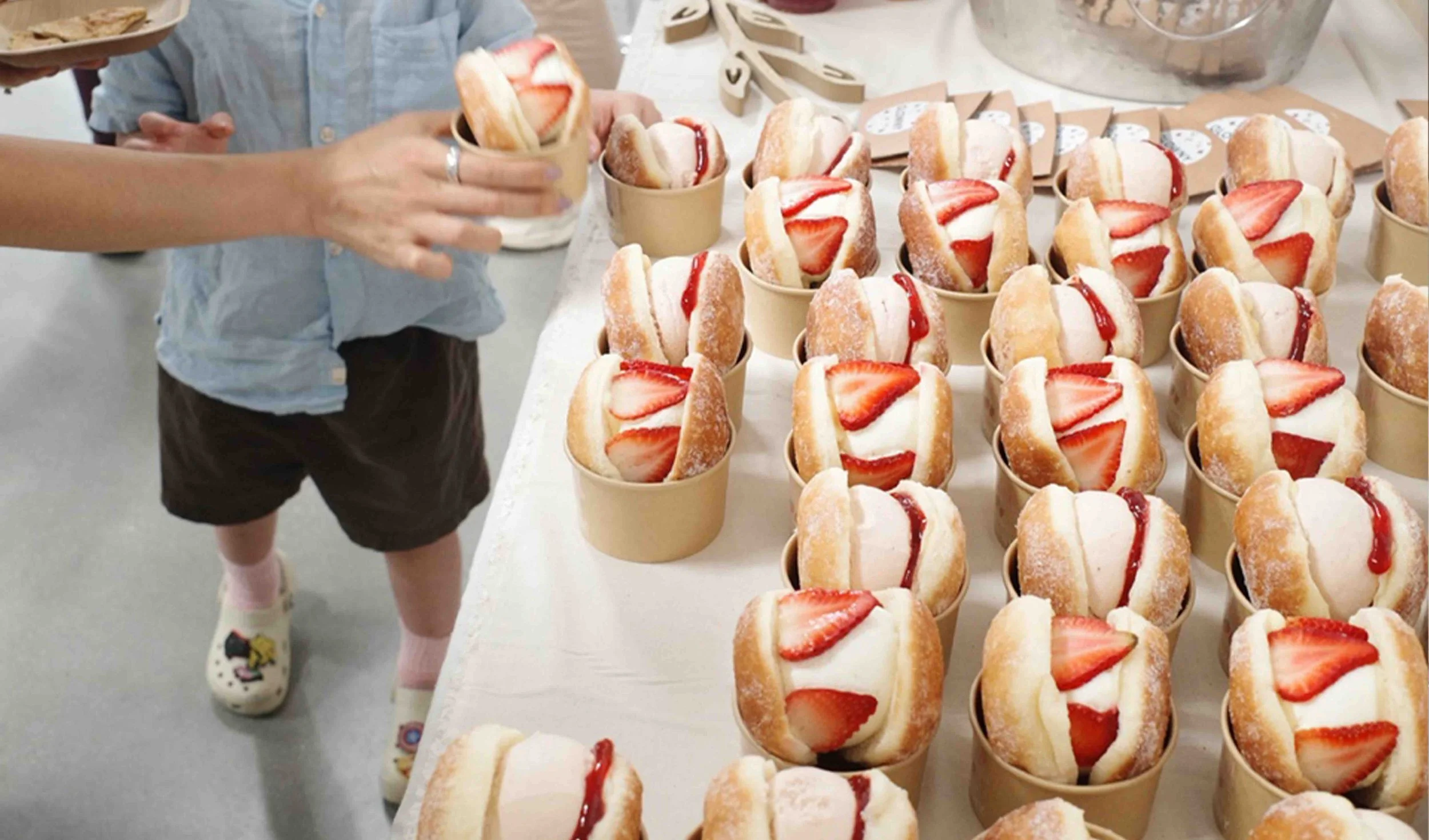 Children reaching for strawberry cream donuts in catering setup