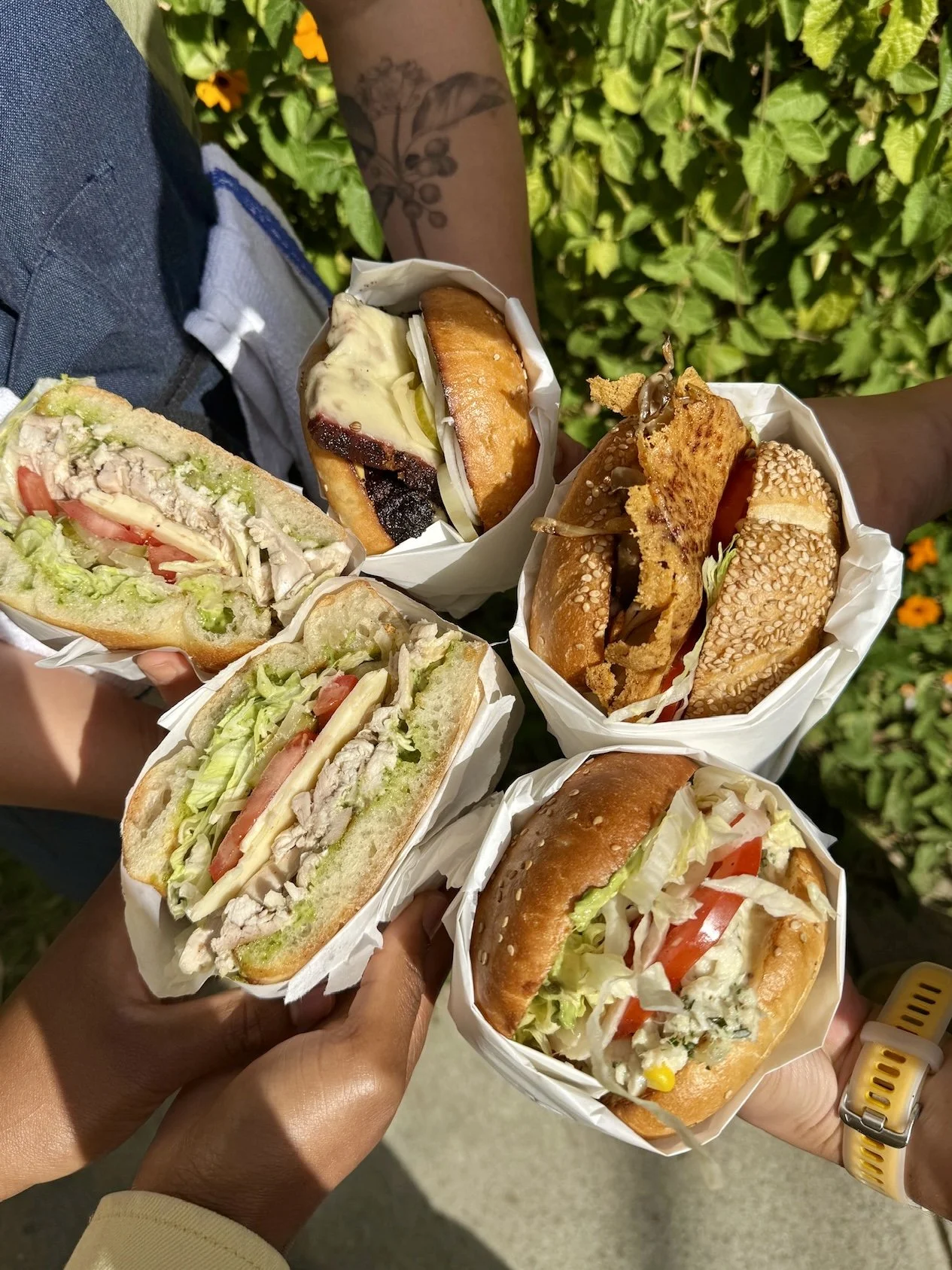 People holding five Rosie’s sandwiches outdoors