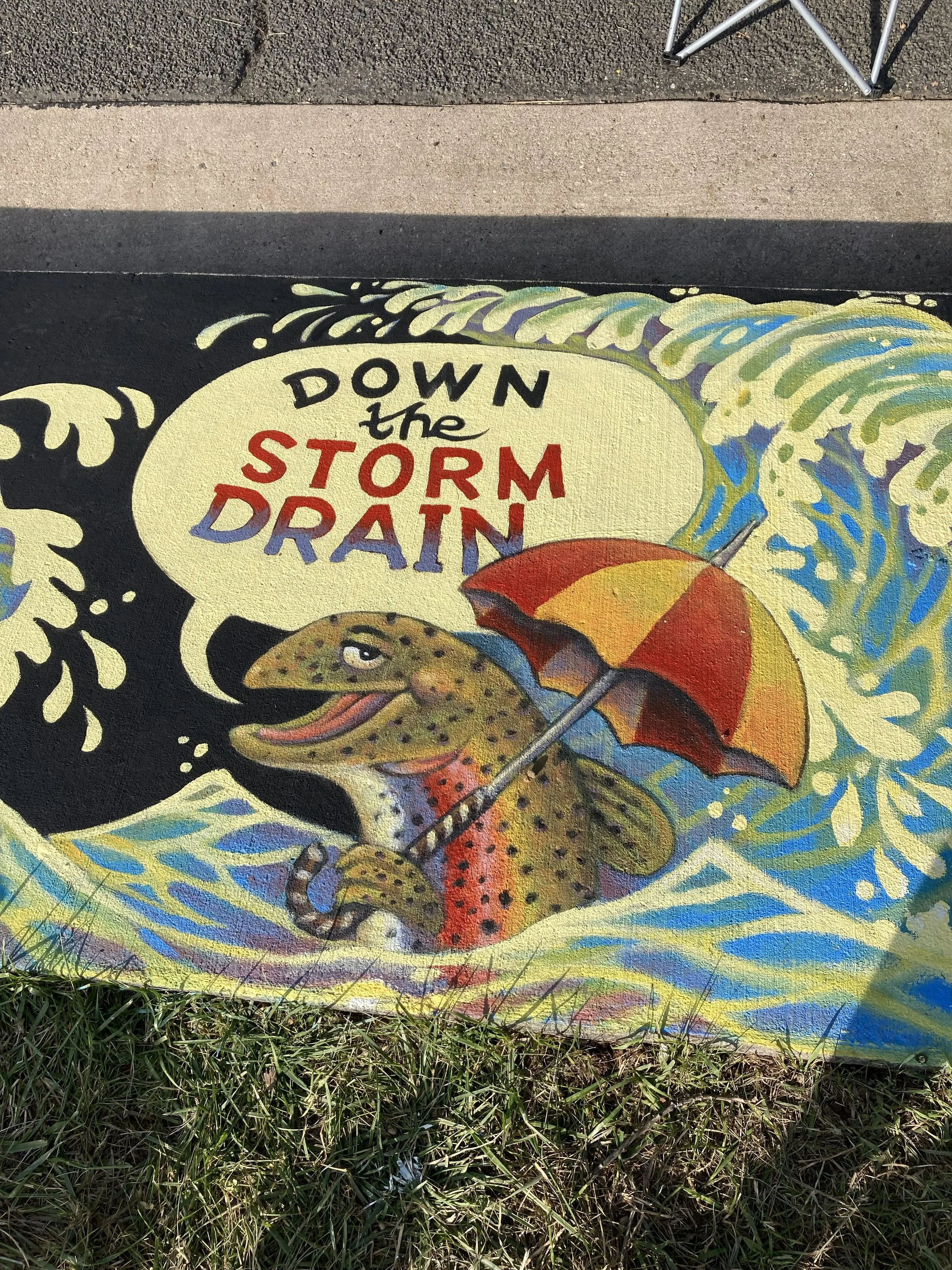 Only Rain in the Drain, 2024, road paint on cement, 5' x 15', commissioned by the City of Fort Collins Art in Public Places