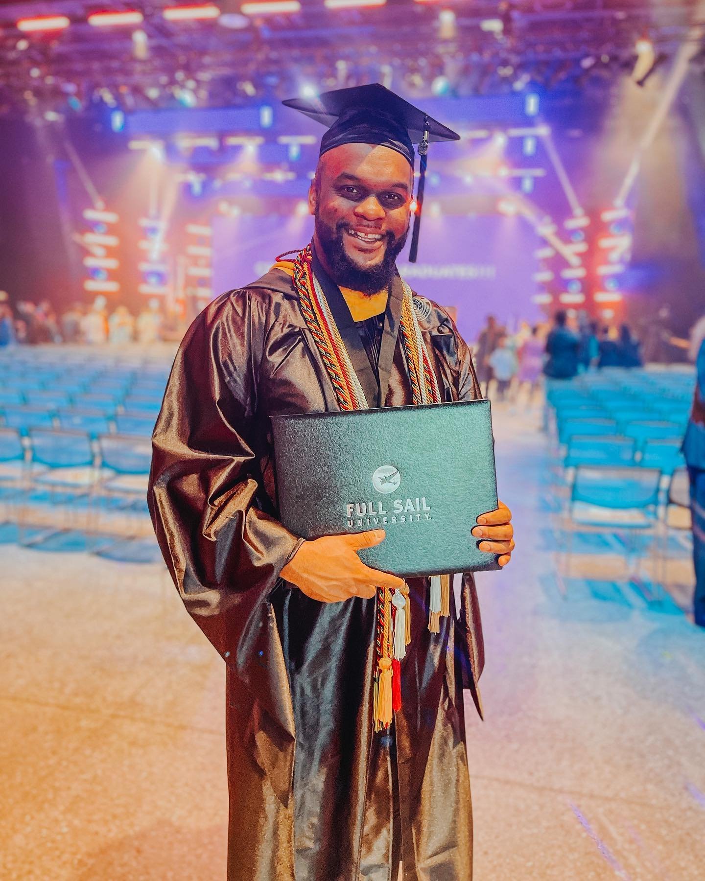 Graduate holding a diploma folder from Full Sail University at a graduation ceremony.