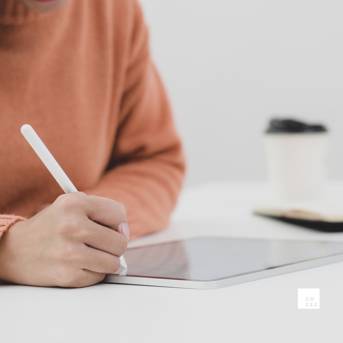 Person using a stylus on a tablet with a coffee cup in the background.