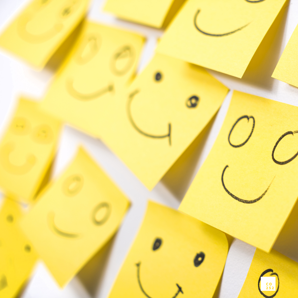 Yellow sticky notes with smiling faces drawn on them, arranged on a wall.