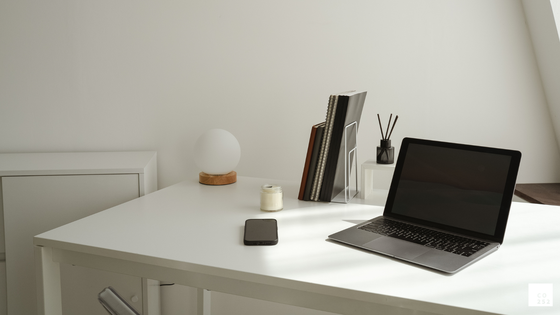 Minimalist workspace with laptop, smartphone, books, and decor items on white desk.