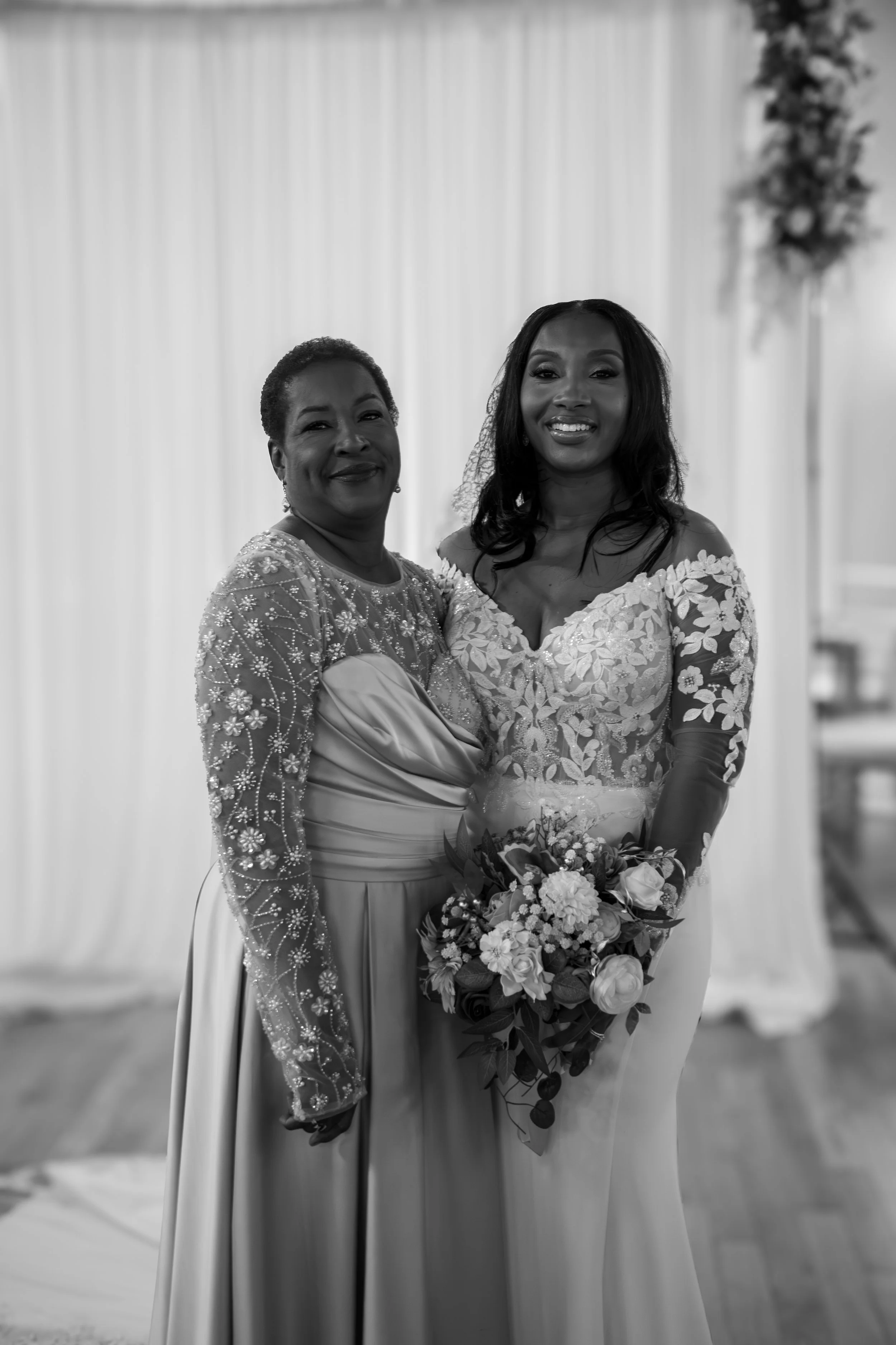 Photo & Video by Will Locke Wedding Photography at the Woman's Club of Portsmouth in Virginia. A black and white photo of two women at a wedding, one in a wedding dress holding a bouquet, and the other in a long, embroidered dress.