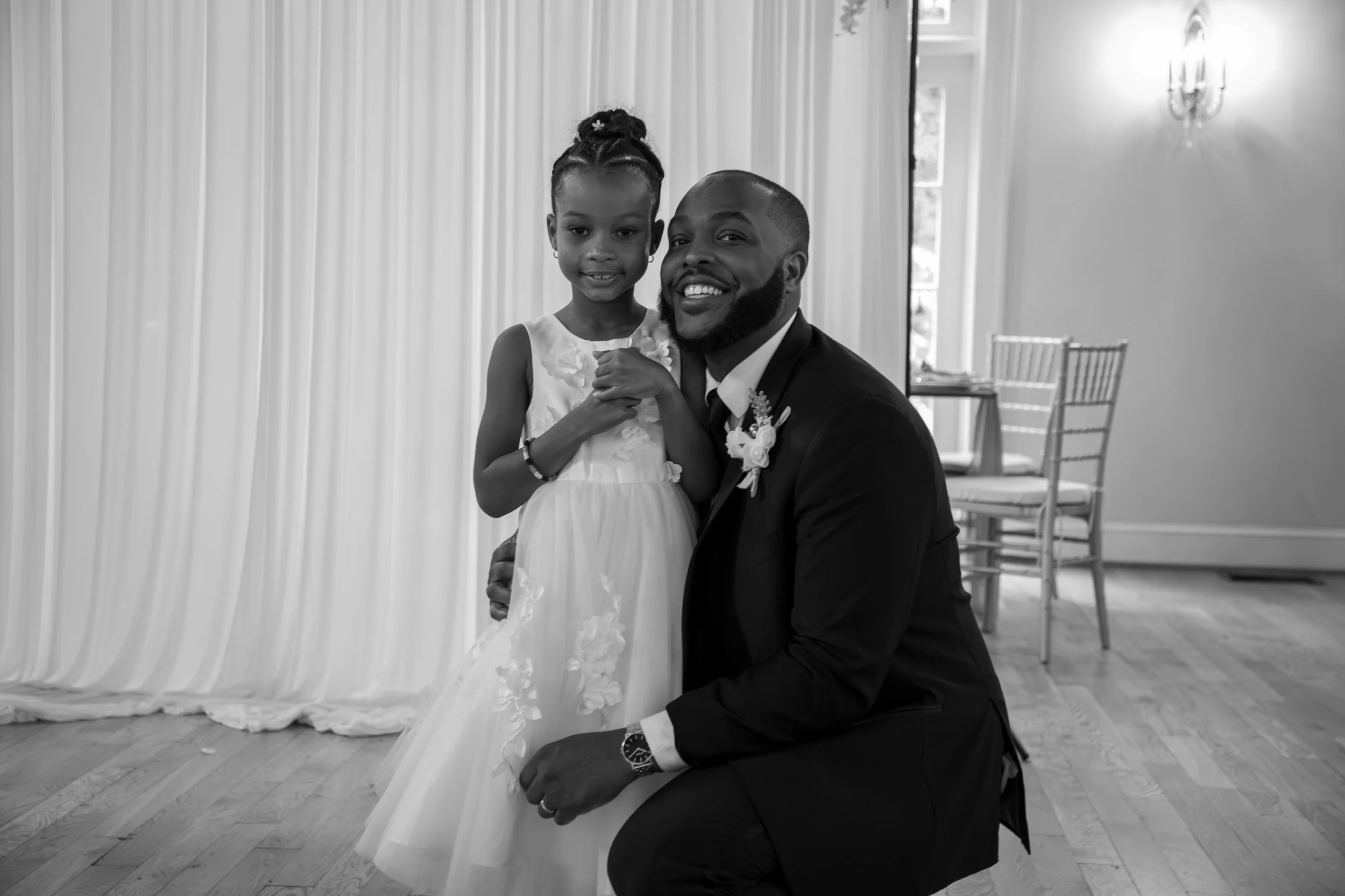 Photo & Video by Will Locke Wedding Photography at the Woman's Club of Portsmouth in Virginia. A man and a young girl dressed in a wedding gown, smiling at the camera in a decorated reception hall.