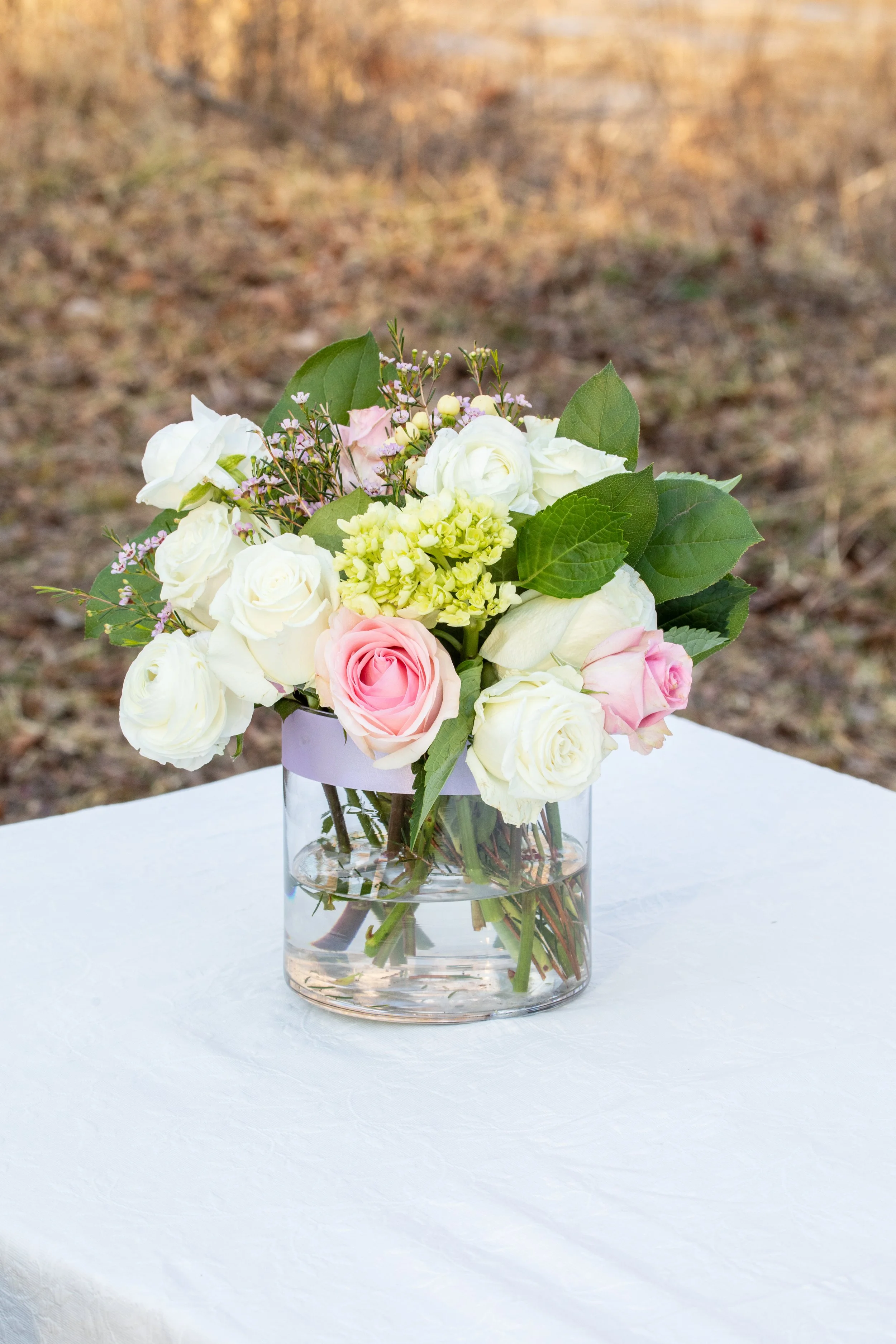 Engagement Photography by Will Locke near Richmond, VA in Montpelier. A flower arrangement sits on a white tablecloth outdoors in the winter with grass behind.