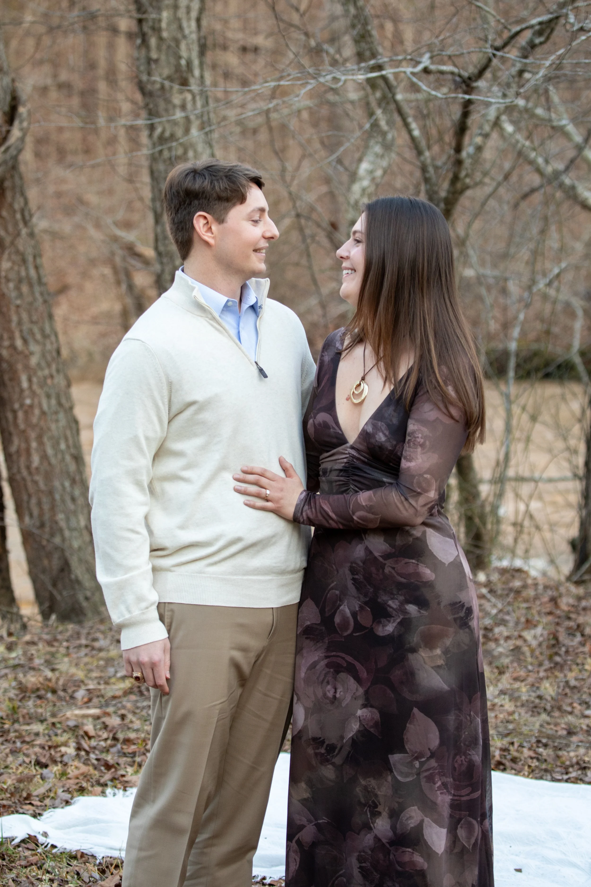 Engagement Photography by Will Locke near Richmond, VA in Montpelier. A man and woman smiling at each other while holding champagne glasses outdoors during sunset, with a table of flowers nearby.